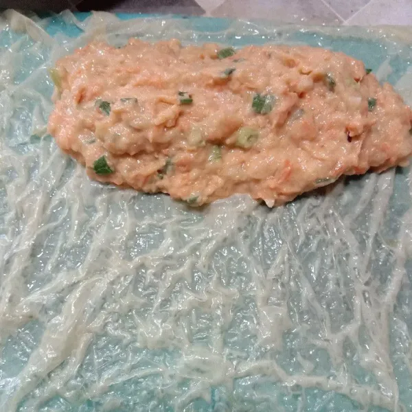 Ambil 2 lembar kulit kembang tahu, celupkan di air. Letakkan di atas talenan, beri satu bagian adonan, lalu gulung.