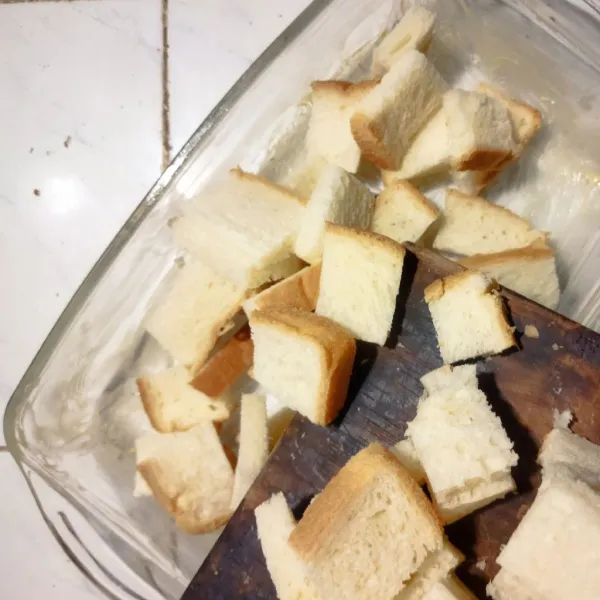 Tata roti tawar yang sudah dipotong di pinggan tahan panas yang sudah dioles dengan margarin.