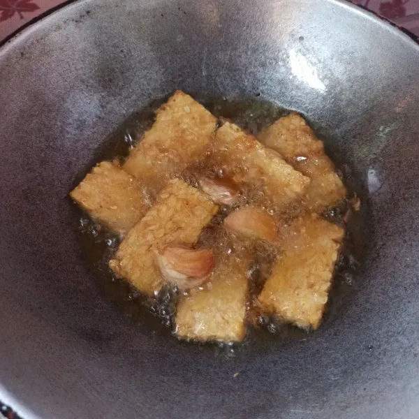 Jika tempe sudah mulai kecokelatan masukkan bawang putih geprek, goreng hingga kering dan matang.