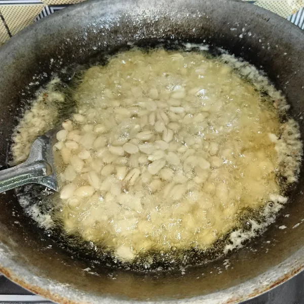 Setelah dua jam tiriskan kacang, lalu goreng kacang sampai matang, angkat dan tiriskan.