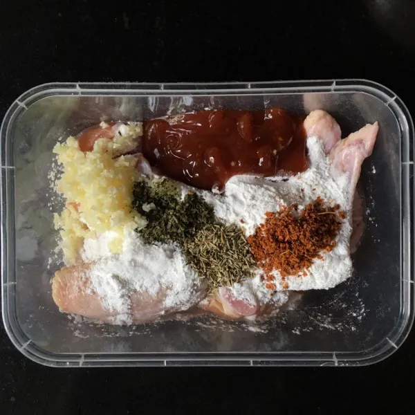 Masukkan sayap ayam ke wadah, tambahkan tepung maizena, saus barbeque, bawang putih cincang, parsley kering, rosemary kering, dan bubuk cabai.