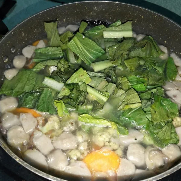 Masukkan sawi hijau dan bakso. Tambahkan garam, penyedab dan kaldu bubuk. Masak kembali hingga matang dan koreksi rasa.