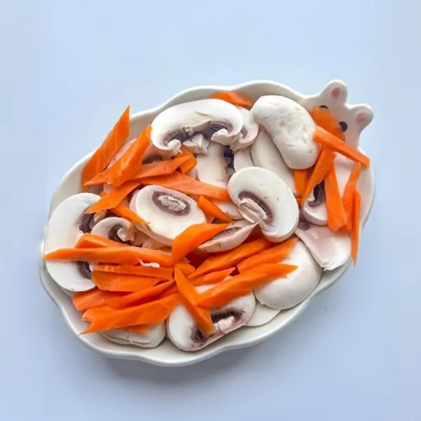 Iris jamur kancing dan wortel, lalu letakkan di dalam mangkuk atau piring tahan panas