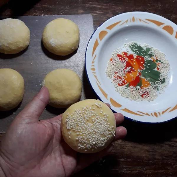 Kempiskan adonan dan bagi menjadi 6. Bentuk bulat dan pipihkan, olesi bagian bawah dan atas dengan air dan taburi wijen.