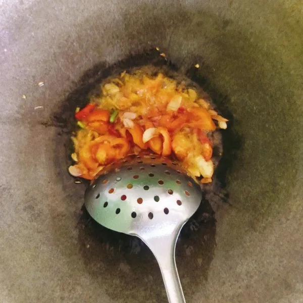 Panaskan sedikit minyak dalam wajan yang sama, tumis bawang putih dan bawang merah hingga harum. Tambahkan tomat, lalu tambahkan cabai merah dan cabai rawit jika digunakan, tumis sebentar.