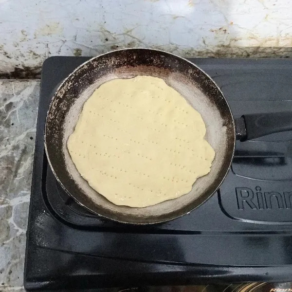 Bagi adonan menjadi dua, kemudian lebarkan di atas teflon, lalu tusuk-tusuk dengan garpu agar adonan matang sempurna.