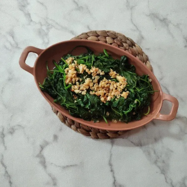 Tata tumis bayam di piring saji. Taburi tumis bawang putih goreng. Sajikan.