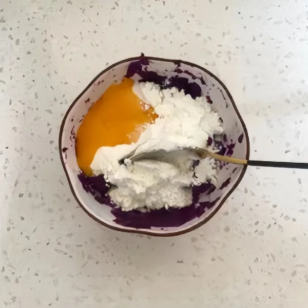 Tambahkan 1 butir kuning telur dan 15 gr tepung rendah gluten ke dalam puree ubi ungu, aduk hingga rata