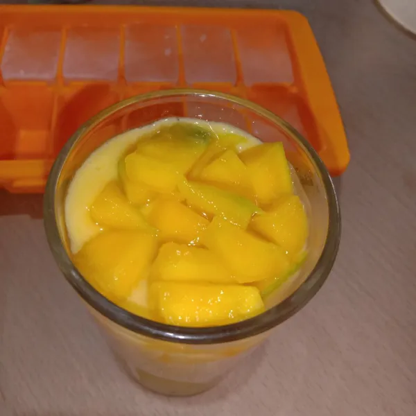 Masukkan es batu ke dalam gelas saji, tuang jus mangga lalu tambahkan potongan mangga di atasnya. Jus Mangga siap di nikmati.