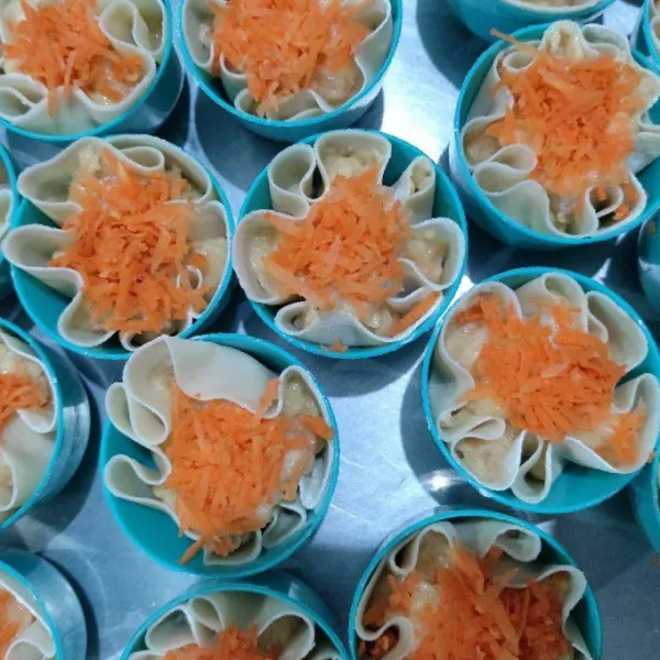 Siapkan kulit pangsit, tuang 1 sdm atau sesuai selera taruh di atas kulit pangsit lalu beri bagian atasnya wortel parut (saya pakai cetakan kue untuk mengukusnya, agar lebih mudah dan area samping kulit bisa nge bentuk dengan sendirinya, lakukan sampai semua adonan habis)