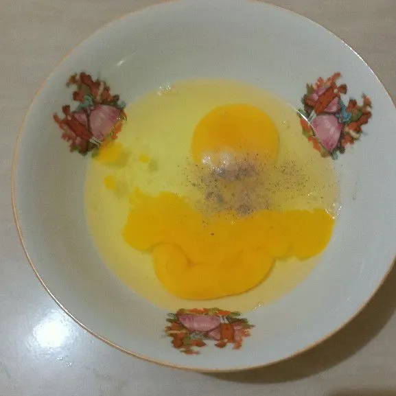 Pecahkan 2 butir telur lalu beri garam dan lada.