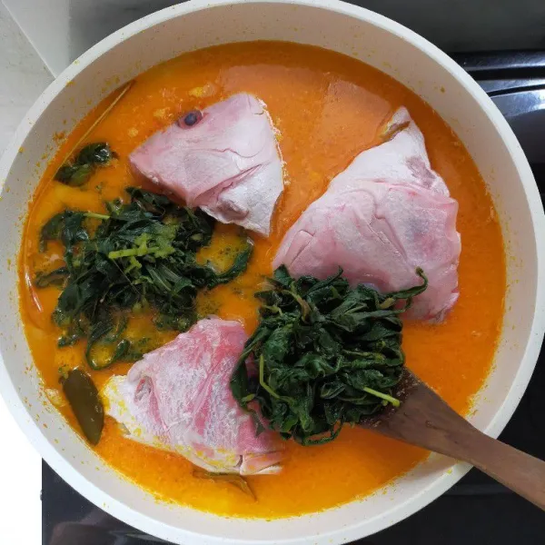 Setelah santan mendidih, masukkan kepala kakap merah dan daun singkong yang sudah di rebus.