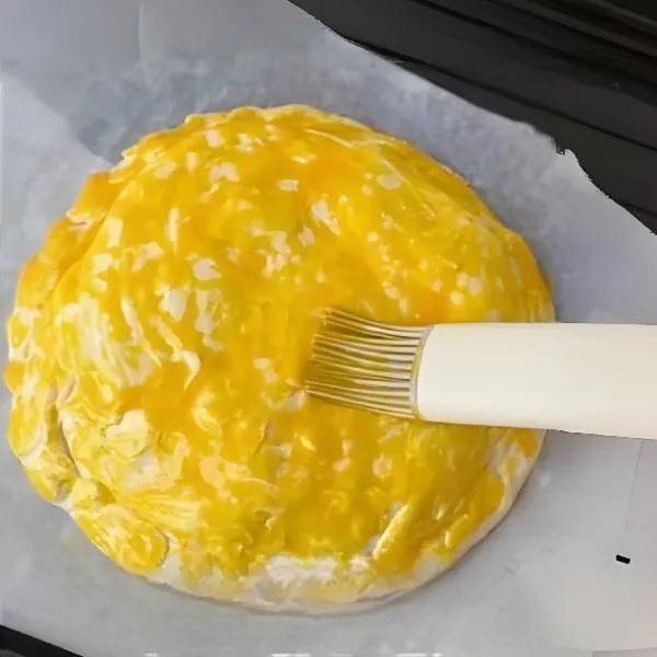 Buat lubang kecil di permukaan dengan garpu, lalu oleskan 1 butir kuning telur yang sudah dikocok di atasnya.