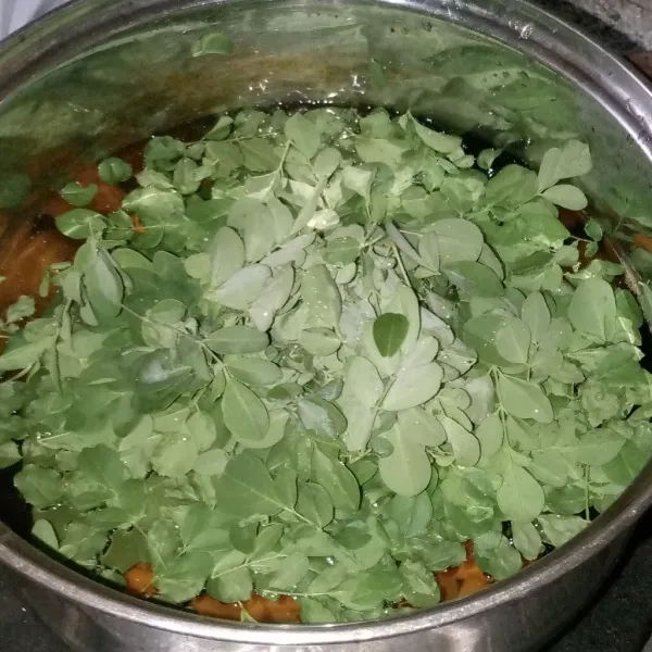 Masukkan daun salam lalu serut daun kelor dan masukkan ke dalam panci. Masak sebentar saja hingga daun terlihat hijau segar. Matikan kompor.