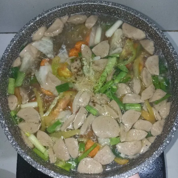 Masukkan tomat, daun bawang, seledri, dan bakso. Lalu tambahkan garam, gula, kaldu bubuk, dan lada. Kemudian, aduk rata.