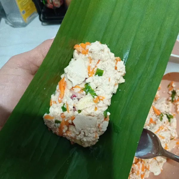 Ambil satu lembar daun pisang. Letakkan dua sendok makan adonan tahu. Kemudian lipat memanjang.