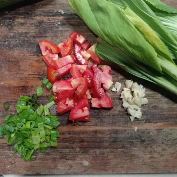 Cincang bawang putih, iris tomat dan daun bawang, buang juga bagian bonggol pakcoy.