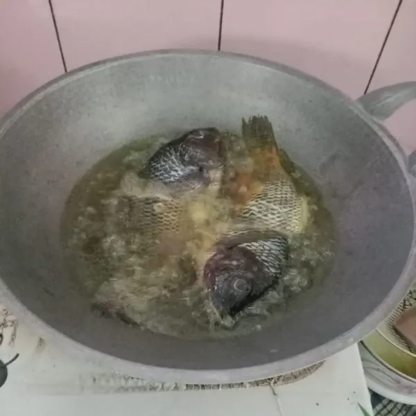 Panaskan minyak, taburi sedikit tepung terigu ke minyak panas (agar tidak meletup), lalu masukkan ikan dan goreng hingga setengah matang.