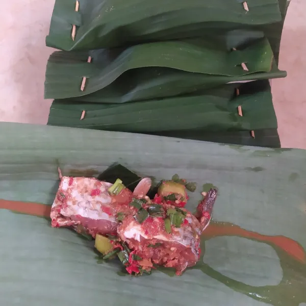 Letakkan daun salam di atas daun pisang. Kemudian, masukkan ikan dan bumbu. Gulung daun pisang, lalu sematkan lidi di bagian atas dan bawah daun pisang. Lakukan hingga habis.