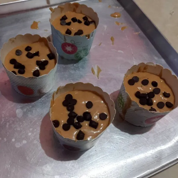Lalu tuang ke cup muffin sekitar 7/8 tinggi cup. Taburi kismis dan choco chips yang disisihkan sebelumnya.