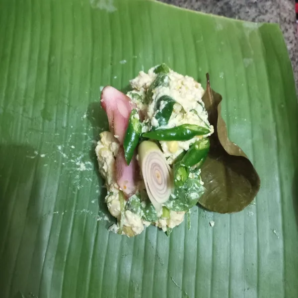 Siapkan daun pisang, tuang adonan tahu, beri daun salam, irisan lengkuas, serai dan cabe hijau keriting, lipat dan rapihkan.