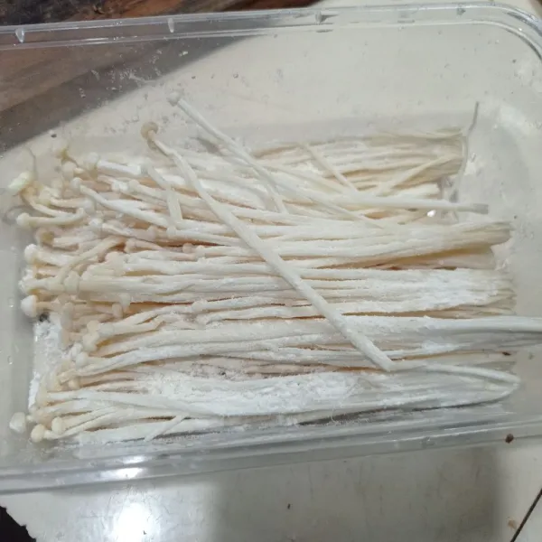 Masukkan jamur enoki ke dalam wadah, lalu beri tepung terigu. Kemudian, aduk rata.