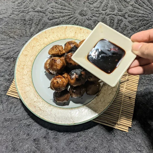 Sajikan bakso bakar di atas piring, lalu siram dengan saus lada hitam.
