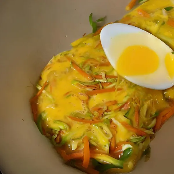 Kocok lepas 3 butir telur, lalu tuang secara merata ke dalam wajan antilengket. Sebelum telur mengeras, susun tumisan wortel dan zucchini di atasnya, lalu ratakan