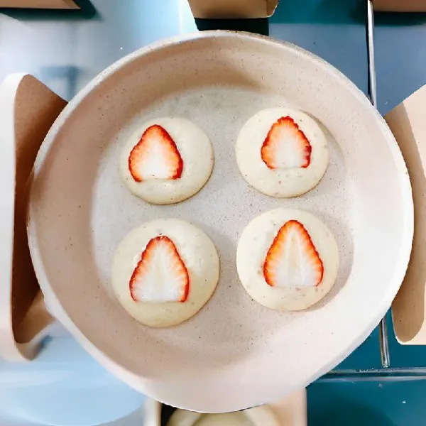 Letakkan 1 iris strawberry di atas setiap pancake. Tutup wajan dan masak selama kurang lebih 3 menit hingga matang sempurna