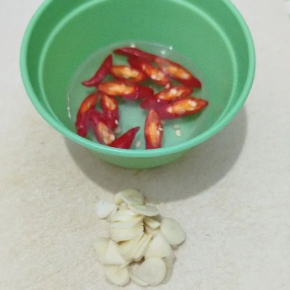 Iris serong cabe keriting merah, rendam dalam air. Iris/cincang halus bawang putih.