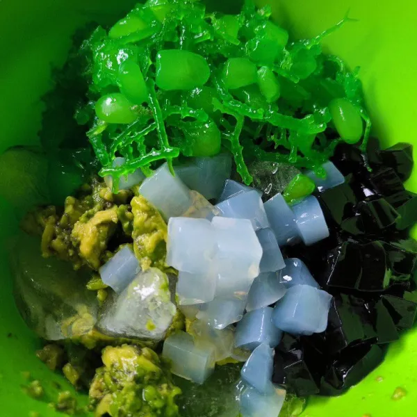 Siapkan wadah, tambahkan es batu yang sudah di hancurkan. Kemudian masukkan alpukat yang sudah dikerok, cincau, nata de coco, kolang kaling dan rumput laut.