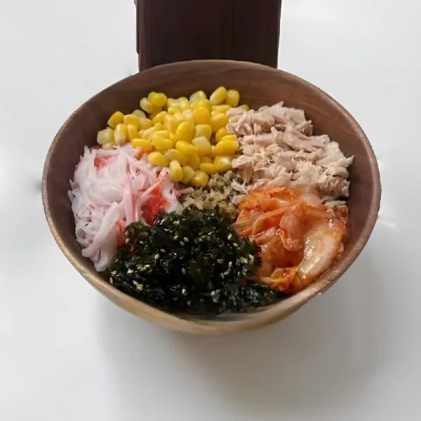 Letakkan quinoa dalam mangkuk sebagai dasar. Tambahkan jagung, tuna, crab stick, kimchi, dan rumput laut di atasnya