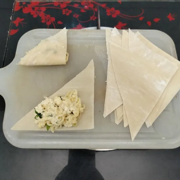 Potong kulit pangsit menjadi 2 bentuk segitiga. Lalu beri isian adonan mie dan lipat.