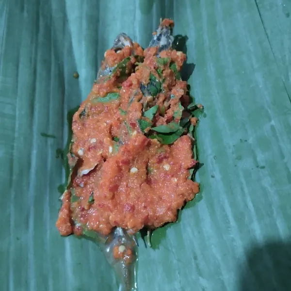 Ambil selembar daun pisang, beri dua ekor ikan pindang dan bumbu halus. Bungkus. Semat ujungnya dengan tusuk lidi.