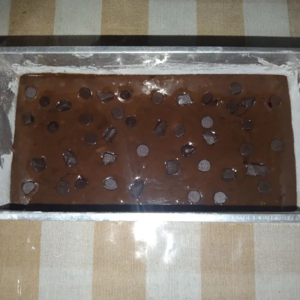 Olesi loyang dengan mentega dan tepung terigu agar adonan tidak lengket lalu taburi topping chocochips diatas adonan