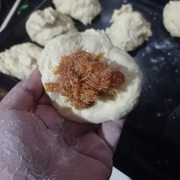 Setelah mengembang kempeskan adonan, bagi jadi 9 bagian, ambil 1 bulatan bagian lalu pipihkan isi dengan unti kelapa