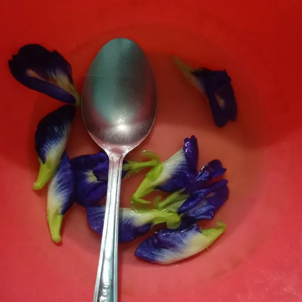 Tuang air panas ke dalam wadah berisi bunga telang, tunggu 10 menit sampai air berwarna biru.