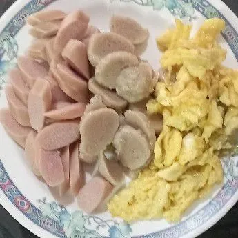 Iris serong sosis dan juga bakso, bikin telur orak-arik.