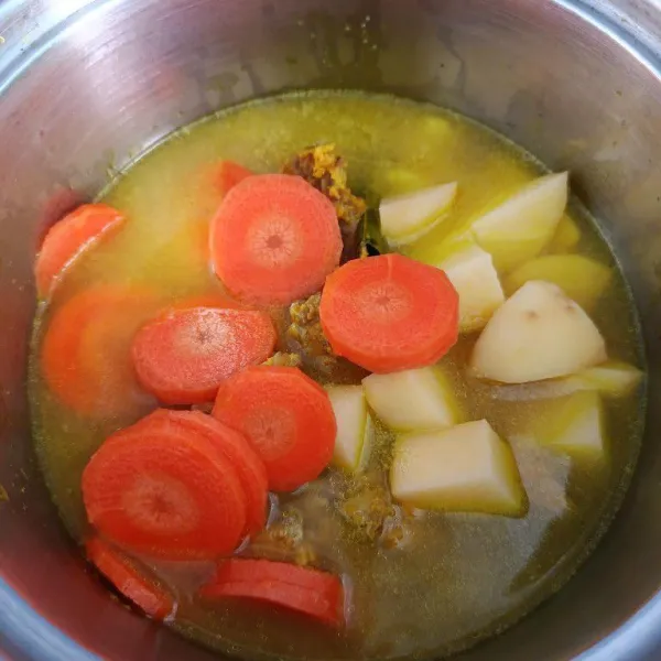 Kemudian pindahkan ke dalam panci, tambahkan air sisa rebusan ayam, potongan wortel dan kentang. Aduk hingga rata.