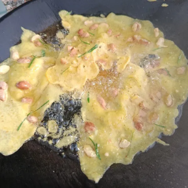 Panaskan minyak agak banyak dalam wajan. Tuang ½ sendok sayur adonan di tepi wajan.