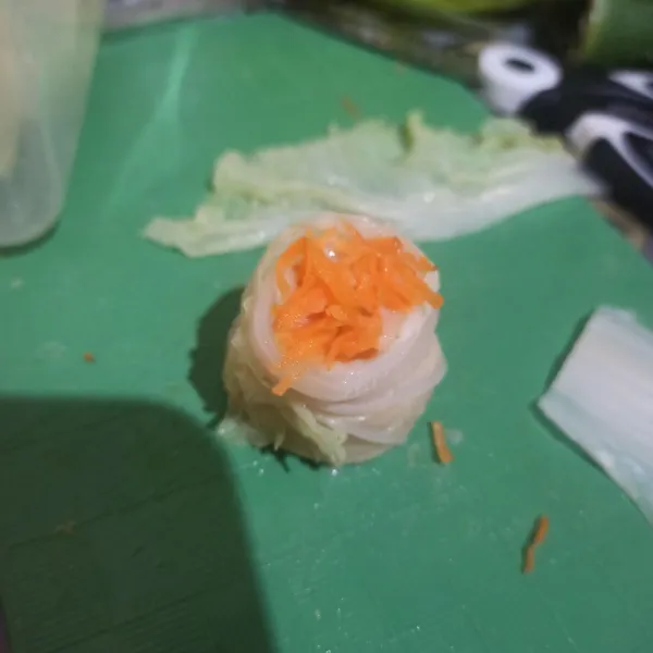 Gulung rapi, lipat bagian bawahnya hingga menutupi adonan, lalu beri taburan wortel parut di atasnya.
