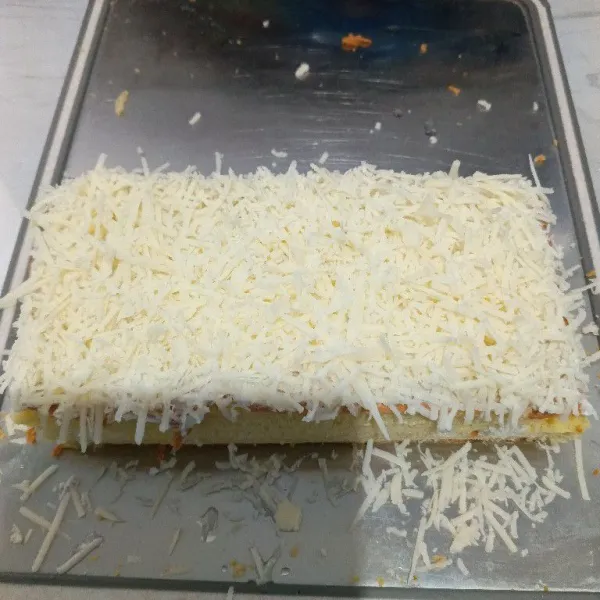 Lalu tumpuk menjadi satu, beri permukaan bolu dengan olesan butter cream, kemudian taburi dengan keju parut. Siap disajikan.