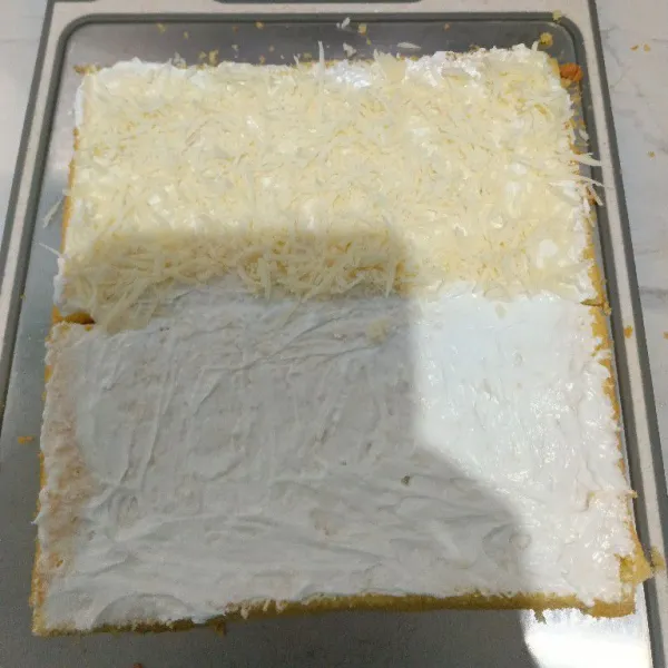 Oles permukaan bolu dengan butter cream, lalu tambahkan keju parut pada satu bagian.