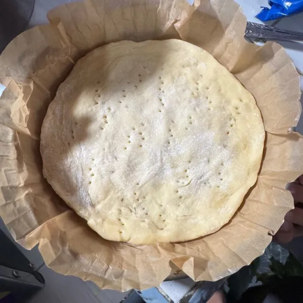 Pipihkan adonan di atas loyang pizza yang sudah dialasi baking paper, tusuk adonan menggunakan garpu, lalu diamkan selama 15 menit.
