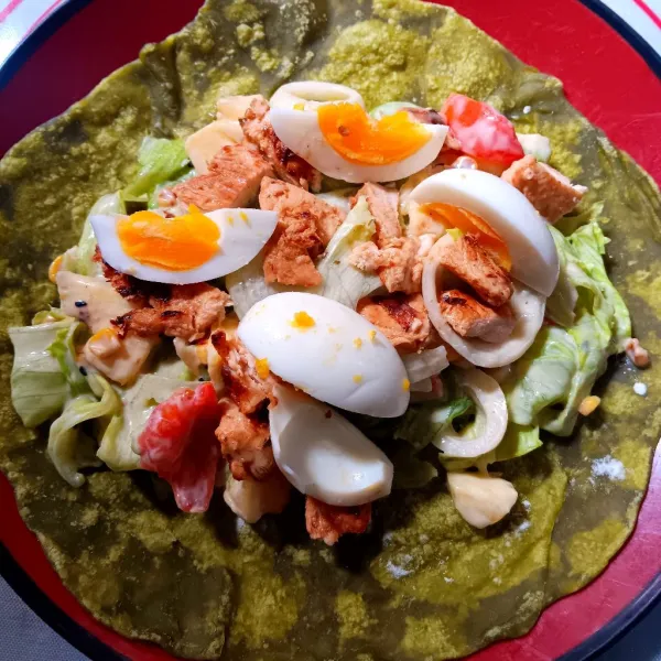 Siapkan selembar tortilla. Beri salad, potongan ayam, dan telur.