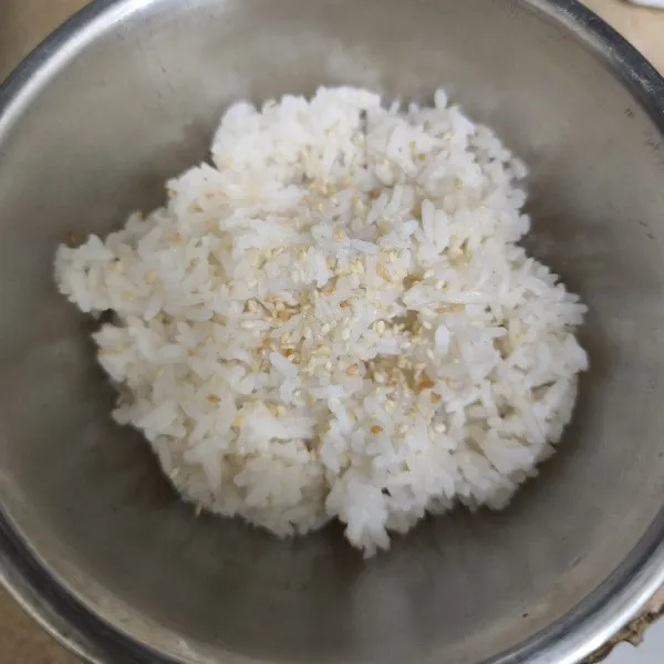 Siapkan nasi panas, tambahkan minyak wijen dan wijen sangrai.