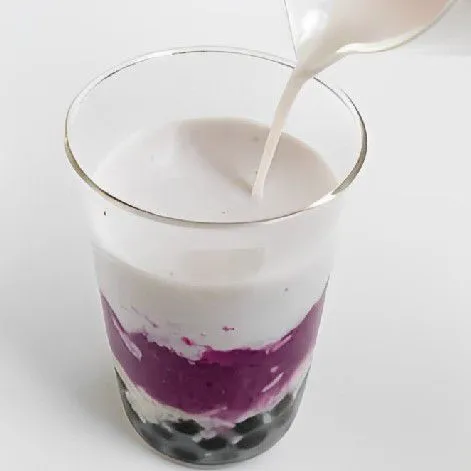 Tuang sisa susu almond yang sudah di hangatkan ke dalam gelas, tepat di atas lapisan boba dan tape ketan.