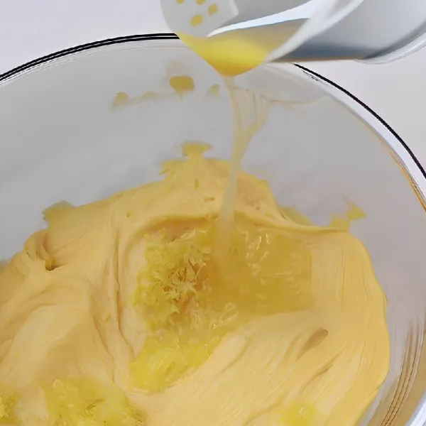 Tuang 100 gr telur yang telah dikocok lepas sedikit demi sedikit ke dalam adonan mentega, aduk rata setiap kali menambahkan.