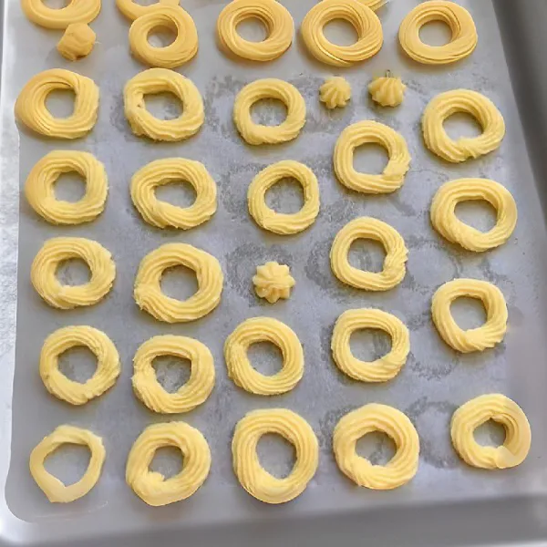 Masukkan adonan ke dalam plastik segitiga (piping bag), lalu semprotkan ke atas loyang yang telah dialasi kertas baking.