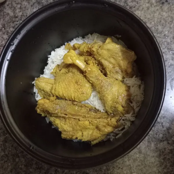 Masukan nasi pada panci magicom, tata potongan ayam matang diatasnya.